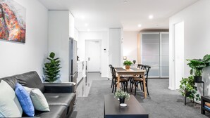 A modern living room with a black leather sofa, a dining table with chairs, and a coffee table with a plant. - Green & Serene - Lush 1BR w Pool & Gym (Melbourne)