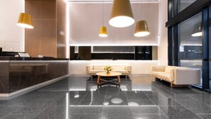 A modern lobby with a reception desk, two sofas, and pendant lighting. - Green & Serene - Lush 1BR w Pool & Gym (Melbourne)