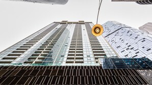 A high-rise building with a modern glass facade and a distinctive golden spherical structure attached to the side. - Green & Serene - Lush 1BR w Pool & Gym (Melbourne)