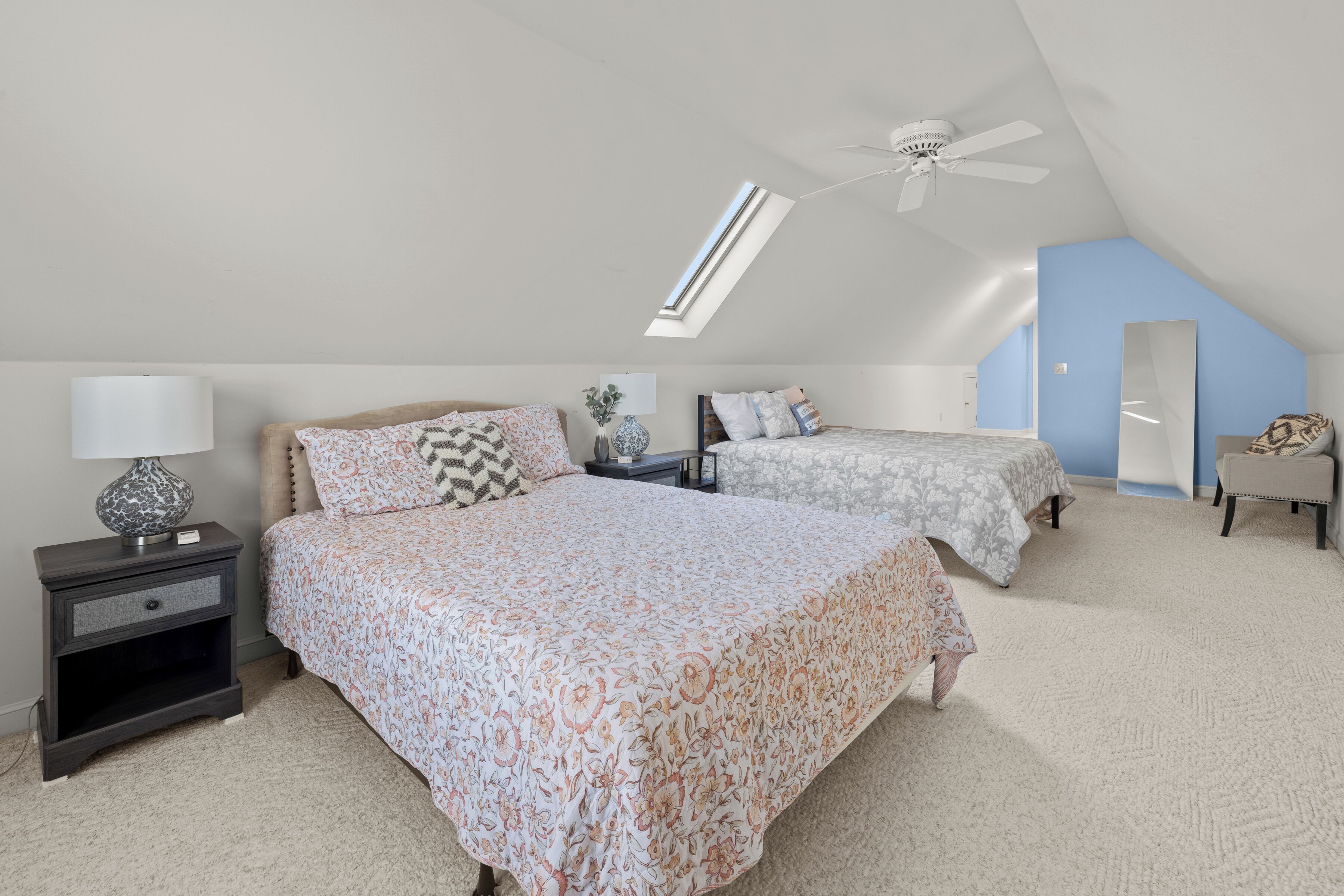 Ein Schlafzimmer mit zwei Betten, einem Deckenventilator, einem Oberlicht und einem Spiegel.