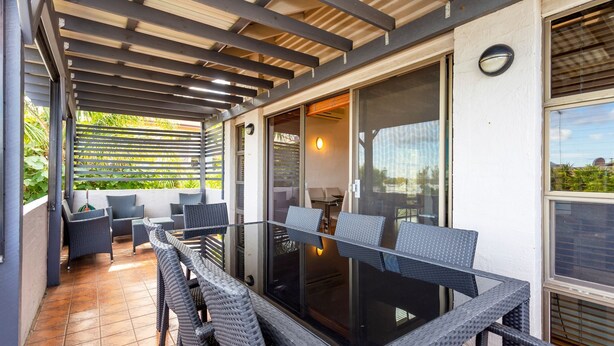 A covered outdoor seating area with wicker furniture and a glass table, overlooking a garden. - Como Mezzanine Retreat (Como)