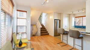 A modern kitchen with a stainless steel refrigerator, a wooden staircase, and a dining area with a yellow chair and a vase of flowers. - Como Mezzanine Retreat (Como)