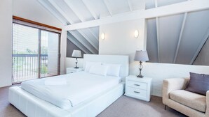 A modern bedroom with a large bed, bedside tables, a nightstand, a sofa, and a window with blinds. - Como Mezzanine Retreat (Como)