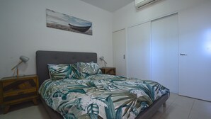 Un dormitorio con cama, dos mesitas de noche, aire acondicionado de pared y una puerta.