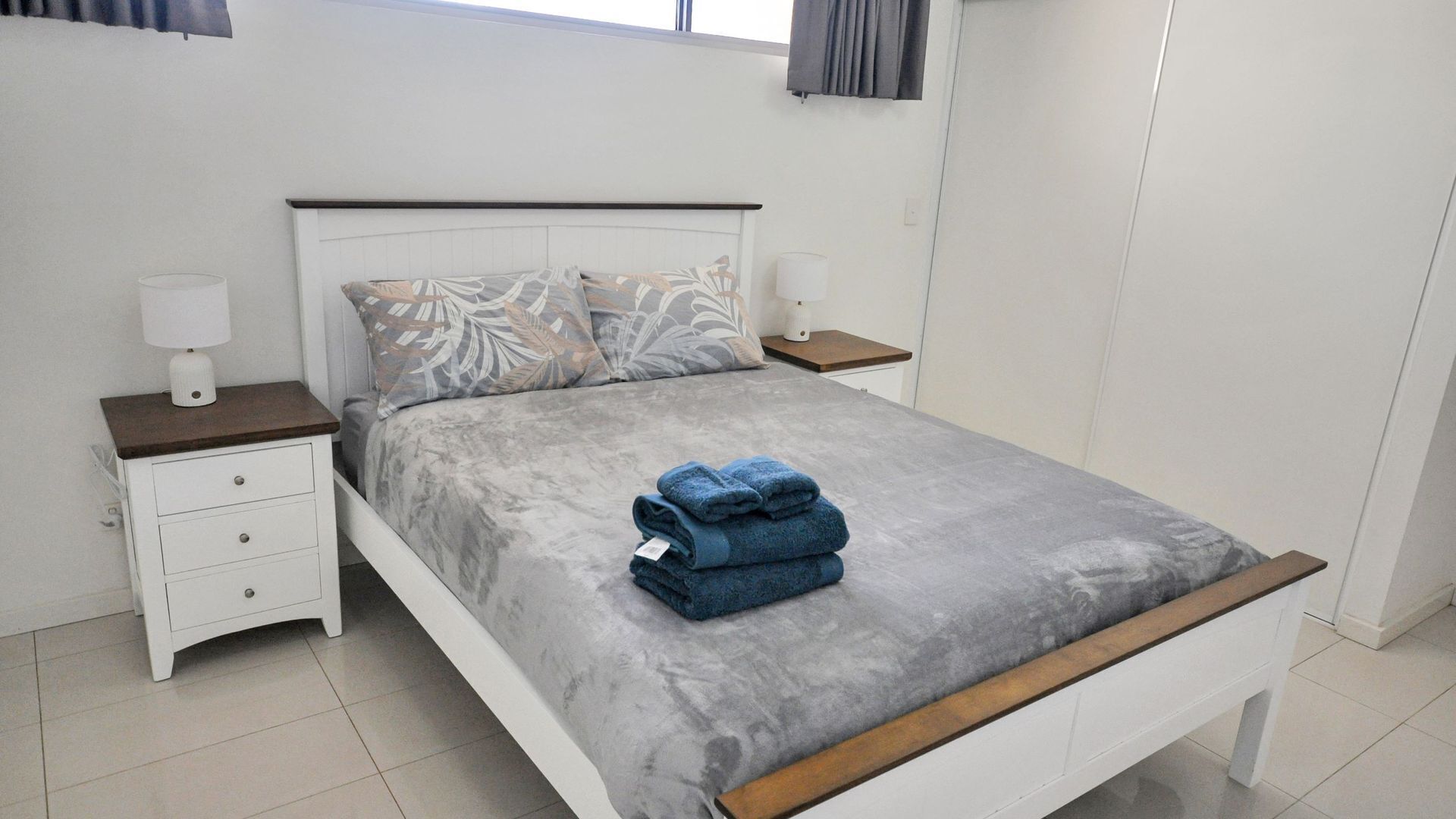 Un letto rifatto con cura, con una coperta grigia e due cuscini, un comodino bianco con una lampada e una testiera in legno.
