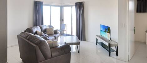 A modern living room with a leather sofa, a coffee table, and a flat-screen TV on a stand.