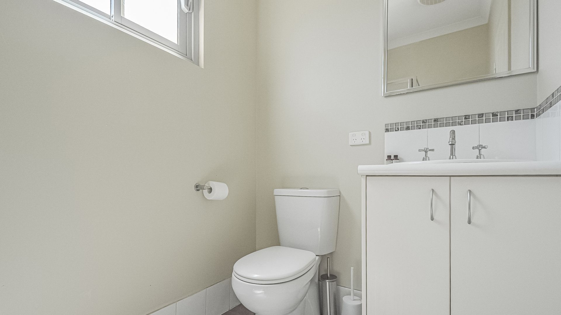 A small, clean bathroom with a toilet, sink, and mirror.