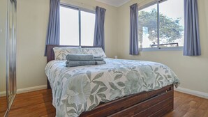A bedroom with a large bed, two windows with curtains, and a view of trees outside. - Marvellous McKay 3x2 Close to CBD (Port Hedland)