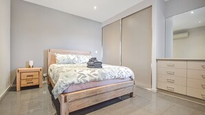 Quarto com cama de madeira, mesa de cabeceira, cômoda e armário de portas deslizantes.