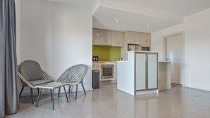 Um apartamento moderno com área de refeições, com duas cadeiras de vime, cozinha com armários claros e um micro-ondas, e uma geladeira branca grande.
