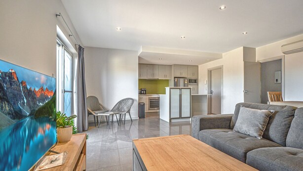 Uma sala de estar moderna com um sofá cinzento, uma mesa de centro de madeira e um quadro de uma paisagem montanhosa.
