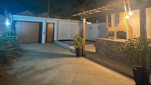 Une maison d’habitation de nuit, avec une allée pavée, un garage, une cheminée en briques et des plantes en pot.