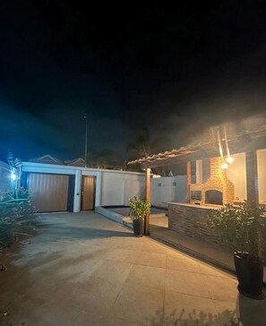 A residential property at night with a paved driveway, a garage, a brick fireplace, and potted plants.