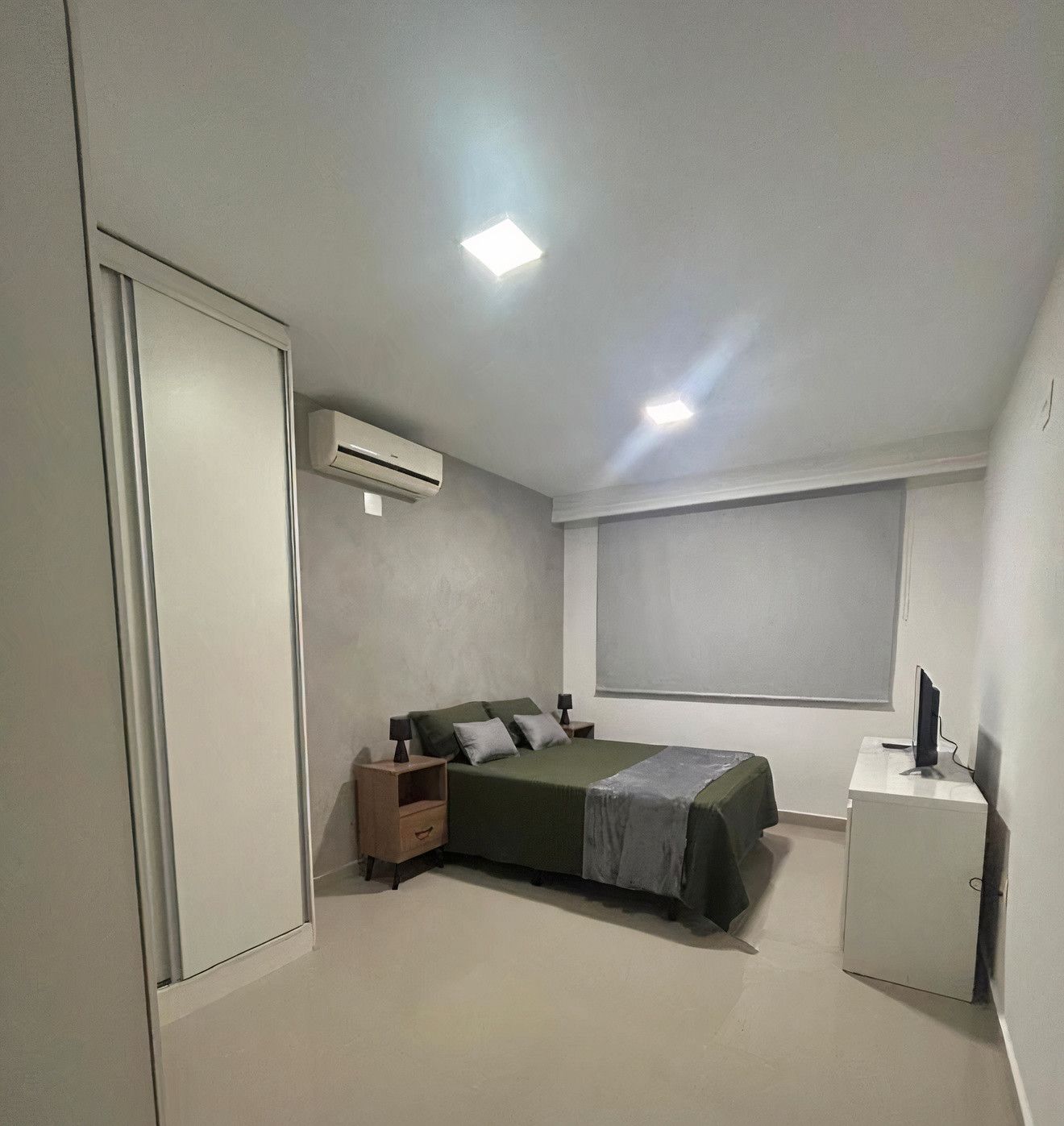 Un dormitorio con cama, mesita de noche y un pequeño armario blanco.