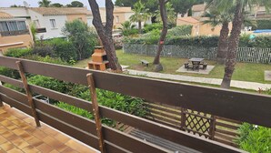 Un balcon doté d’une balustrade en bois, d’un sol carrelé et offrant une vue sur un jardin bien entretenu, avec des palmiers, un espace barbecue et une piscine.