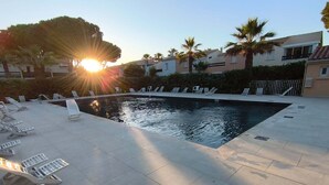 Une piscine à l’eau scintillante sous le soleil, entourée de chaises longues et de palmiers, avec en arrière-plan des immeubles d’habitation.