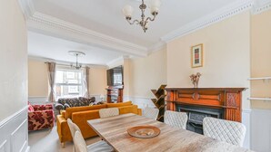 A dining area with a wooden table and chairs, a fireplace, and a sofa set. - Your Spacious South East Sanctuary | Fast City Links (London)