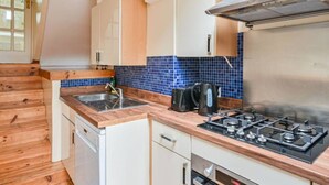 A compact kitchen with wooden flooring, a gas stove, a dishwasher, and a blue-tiled backsplash. - Your Spacious South East Sanctuary | Fast City Links (London)