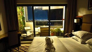 Ein Hotelzimmer mit Bett, Stuhl, Schreibtisch und Blick auf eine Stadtlandschaft durch ein großes Fenster.