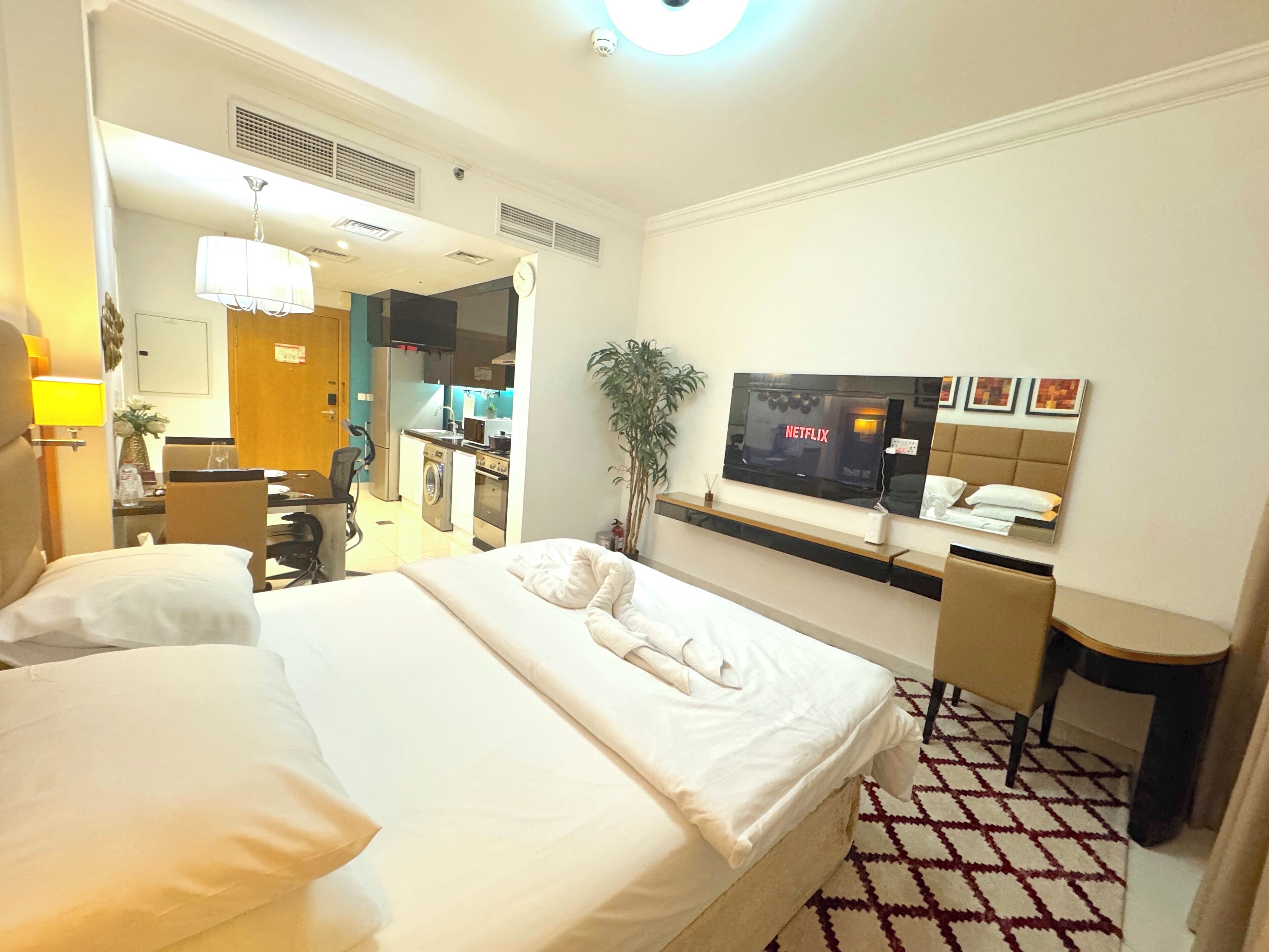 A hotel room with a bed, a desk with a computer, a TV, and a small kitchenette.