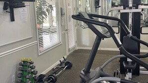 A gym with exercise equipment, a TV, and windows with blinds.
