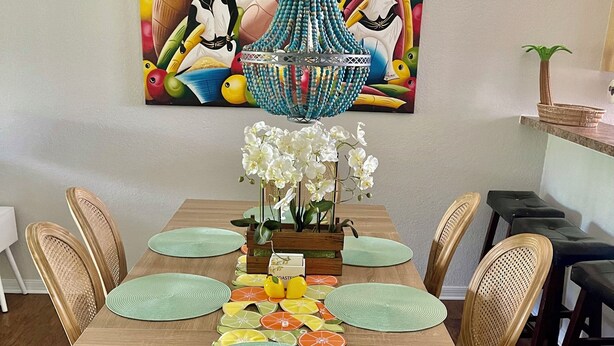 A dining room with a wooden table, wicker chairs, and a colorful abstract painting above.