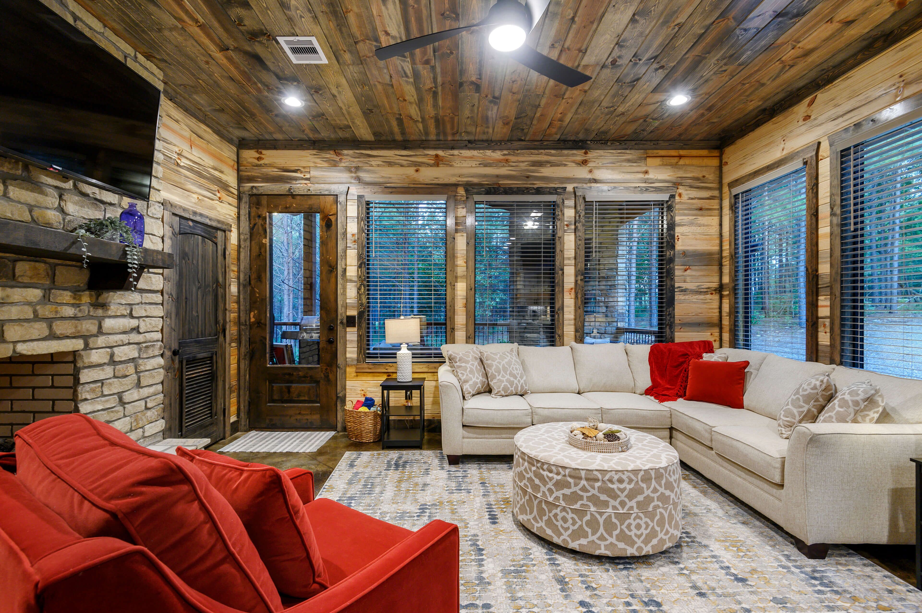 A cozy living room with a fireplace, a sofa, a red chair, and a patterned ottoman.