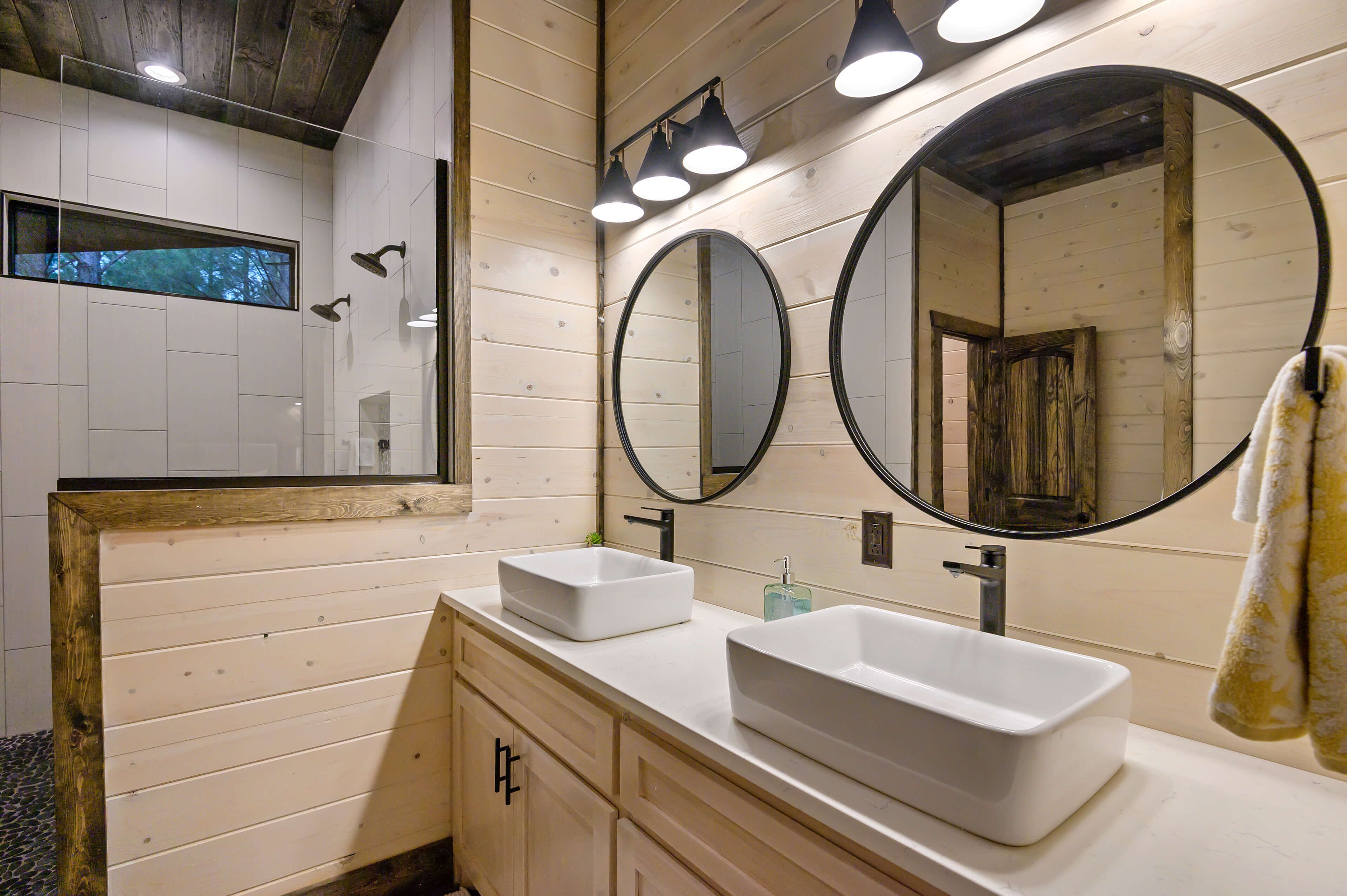 A modern bathroom with two white sinks, a large mirror, and a shower area.