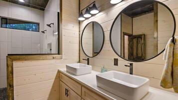 A modern bathroom with two white sinks, a large mirror, and a shower area.