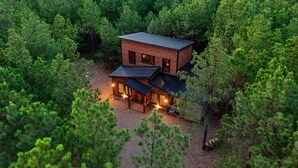 Una cabaña moderna rodeada de un bosque frondoso, con una amplia terraza y varios ventanales.