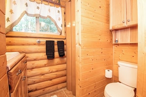 A wooden cabin bathroom with a toilet, towel rack, and wooden cabinets. - Cozy 2-bedroom cabin in tranquil Brian Head (Brian Head)