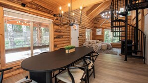 L’intérieur d’une cabane en rondins comprend une table à manger, des chaises, un lustre, un escalier en colimaçon et de grandes fenêtres.