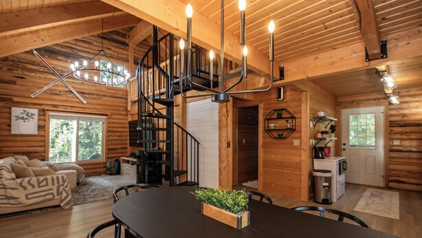 L’intérieur d’un chalet en bois comprend une table à manger, des chaises, un escalier et un lustre.