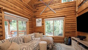 L’intérieur d’une cabane en rondins, avec un canapé d’angle, un pouf et un téléviseur à écran plat.