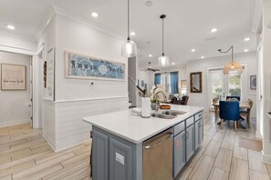 A kitchen with a central island, pendant lights, and a dining area with a table and chairs.