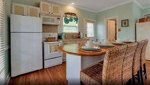 A compact kitchen with a central island, white appliances, and a dining area with wicker chairs.