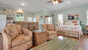 A spacious living room with a sofa, chairs, a coffee table, and a bed with a floral bedspread.