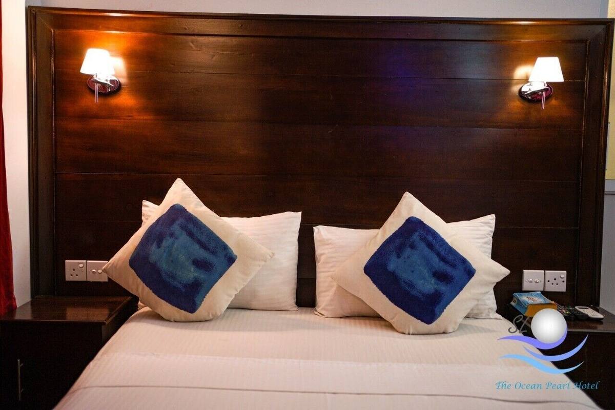 A hotel room with a dark wood headboard, two bedside lamps, and a bed with white bedding and blue diamond-patterned pillows.