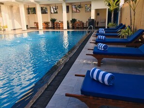 Una piscina con sillas de descanso y mesas, rodeada de muros y plantas en macetas.