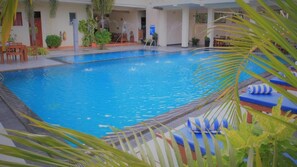 Piscina con sillas de descanso y una zona cubierta con mesas y sillas.