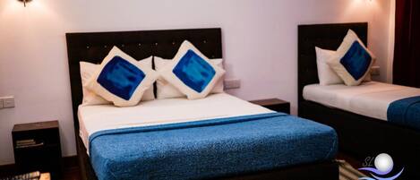 A hotel room with two beds, each with a headboard and pillows. There are bedside tables and a nightstand with a remote control.