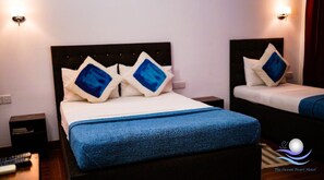 A hotel room with two beds, each with a headboard and pillows. There are bedside tables and a nightstand with a remote control. - The Ocean Pearl Hotel Negombo (Kochchikade)