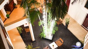 An indoor atrium with a central water feature, surrounded by wooden seating and potted plants. - The Ocean Pearl Hotel Negombo (Kochchikade)