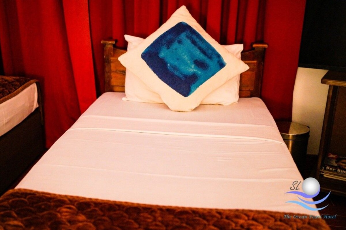 Una habitación de hotel con una cama, una mesita de noche y una cortina roja.