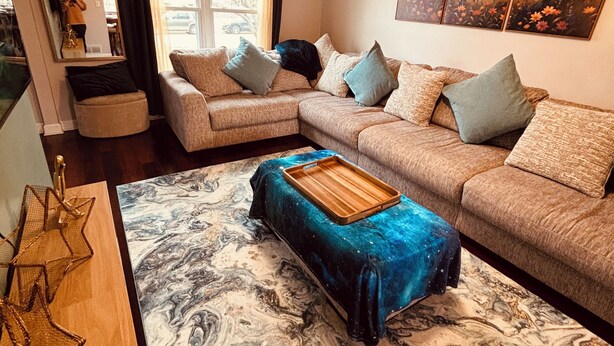 A living room with a sectional sofa, a star-shaped coffee table, a large painting, and a window with curtains. - Galactic Oasis Theme Home,  Marvelous 5-bedroom house with AC in Aurora, TV’s (Aurora)