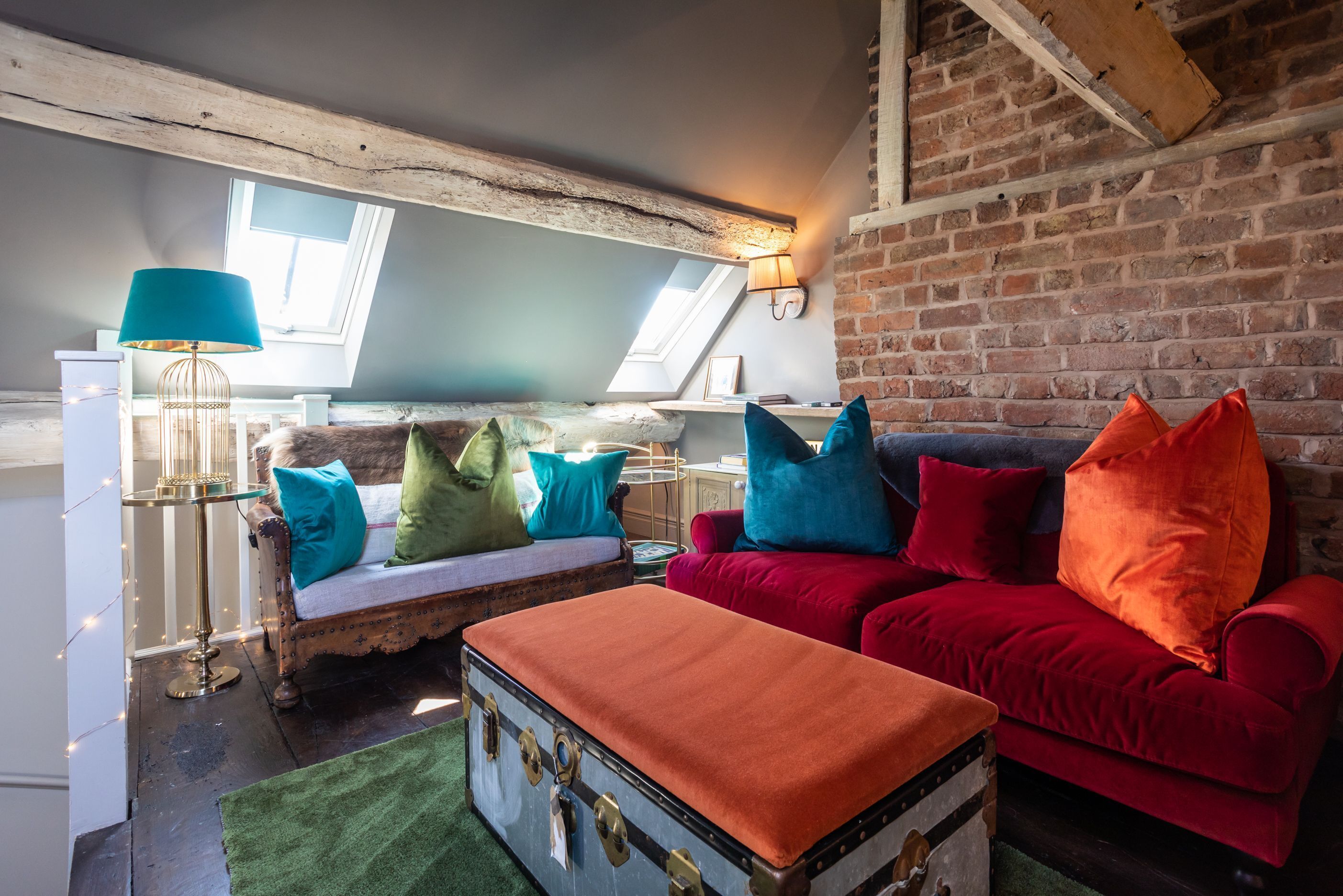 Une pièce de style loft avec des poutres en bois apparentes, un canapé rouge, une malle ancienne et un tapis vert.