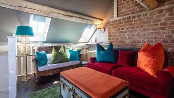 Une pièce de style loft avec des poutres en bois apparentes, un canapé rouge, une malle ancienne et un tapis vert.