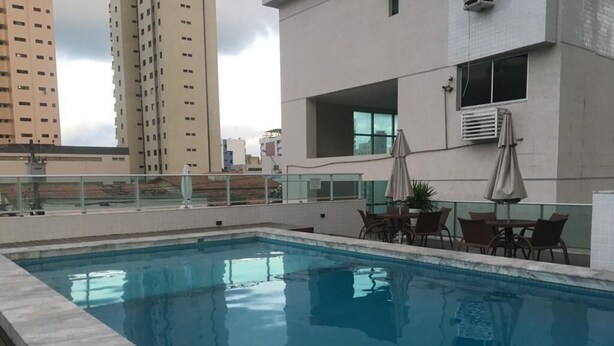 Una piscina con cubierta de madera, mobiliario exterior y vistas a edificios altos.