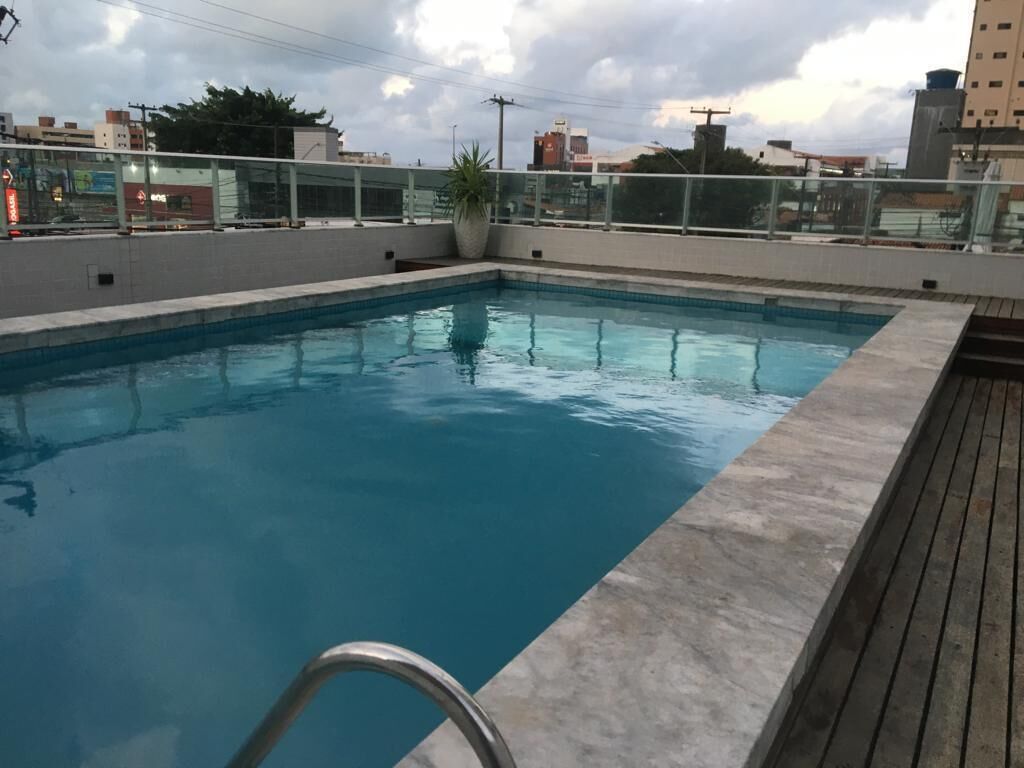 Una piscina sul tetto con una scala in metallo, circondata da una ringhiera in vetro e un pontile in legno.