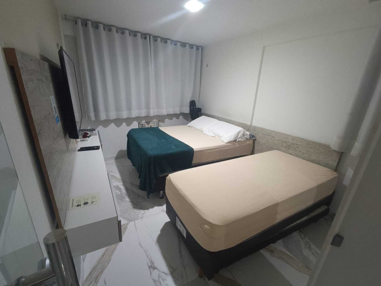 A hotel room with two single beds, a desk with a chair, a flat-screen TV, and a window with curtains.